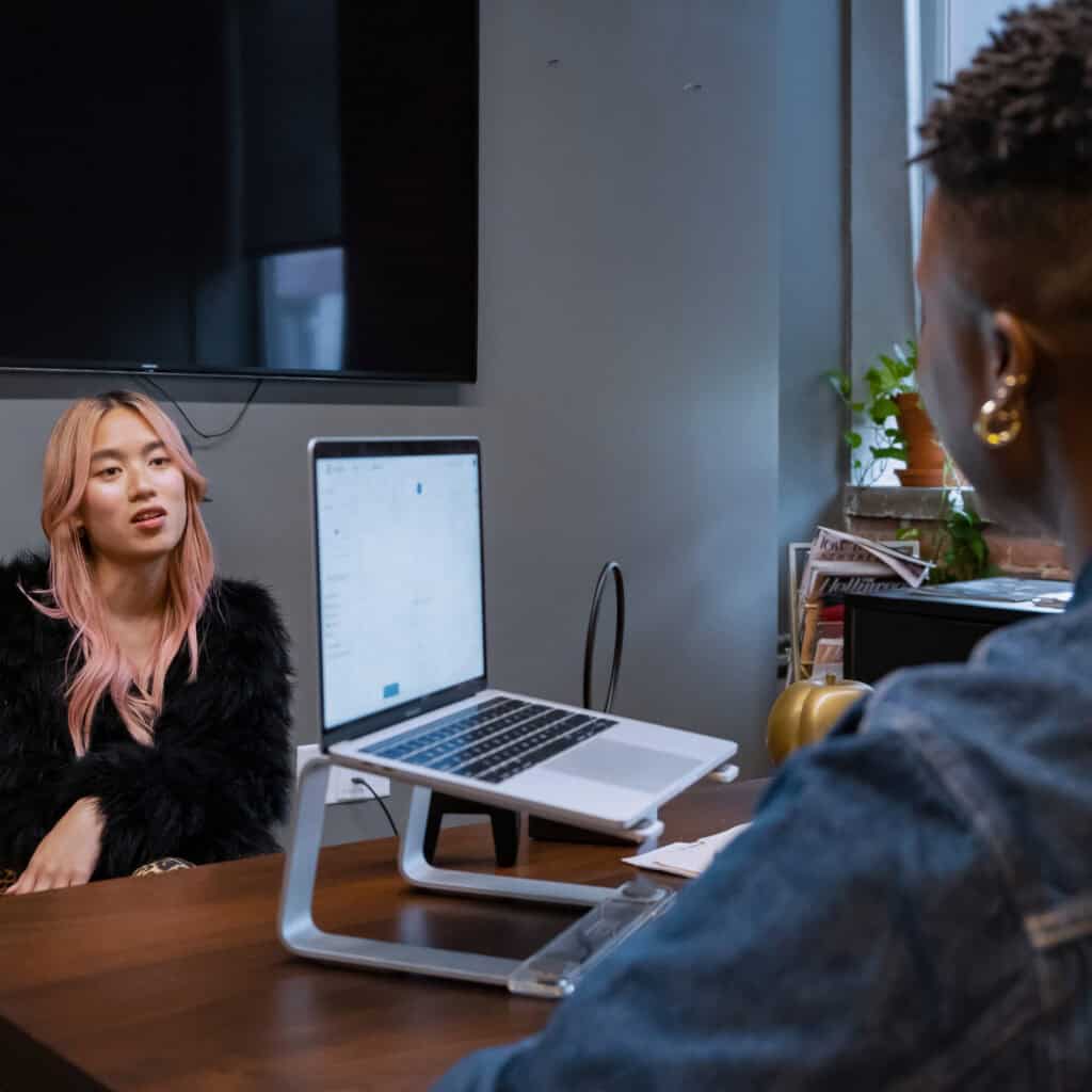 A transfeminine person and a nonbinary person talking in an office.